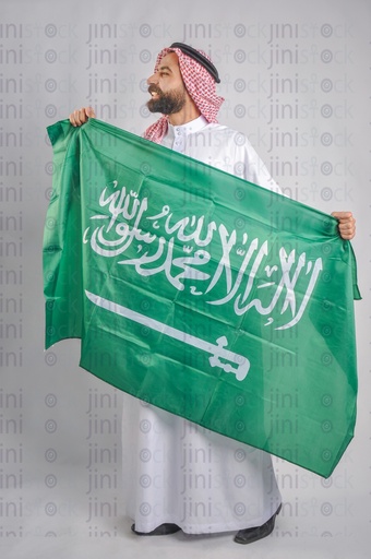 A Saudi man smiling and holding the Saudi Arabian flag with his hands to celebrate the Saudi founding day