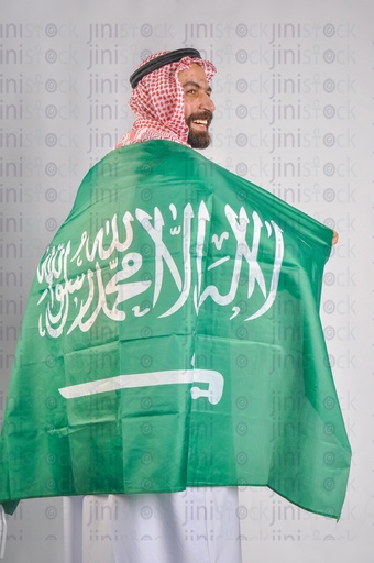 A Saudi man smiling and wearing the Saudi Arabian flag to celebrate the Saudi founding day.