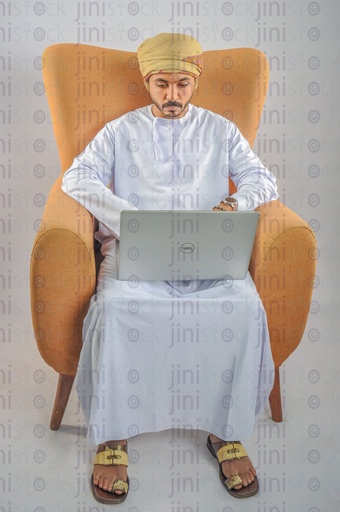 An Omani man sitting on a chair and working on a laptop