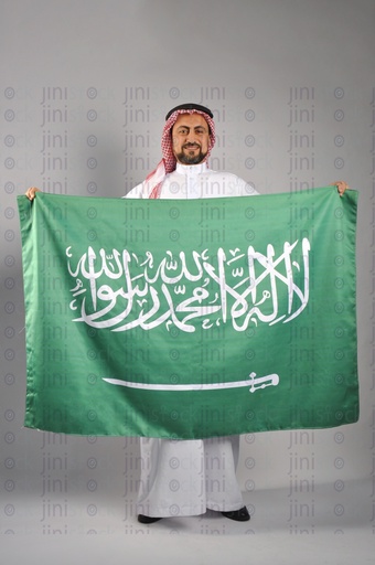 Saudi Arabian man smiling and holding the Saudi Arabian flag in his hands to celebrate the Saudi founding day.