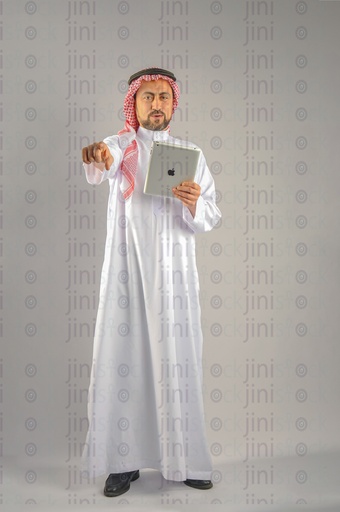 Khaliji Saudi Arabian or Emirati man or a man from the Gulf holding a tablet computer and looking at the camera and pointing at something in front of him.