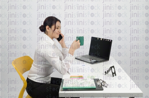 Woman working on laptop and talking on mobile phone - smiling - close-up - stock image