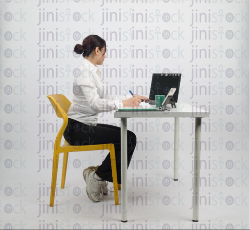 Woman sitting at desk - writing - working on laptop - close side shot - stock image