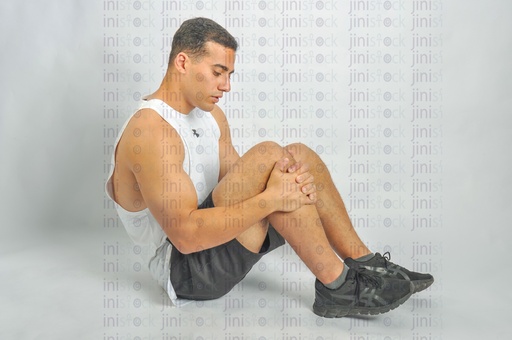 An athletic man sitting on the land and has a leg or knee injury