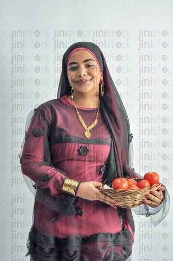 An Egyptian farmer girl or a Nubian woman from Egypt wearing Nubian clothes and holding a plate of tomatoes in her hands