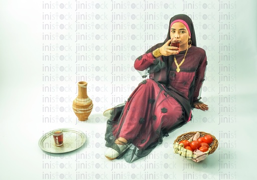 A Nubian Egyptian woman wearing a Nubian dress, a veil on her head, sitting on the land, and drinking a cup of tea