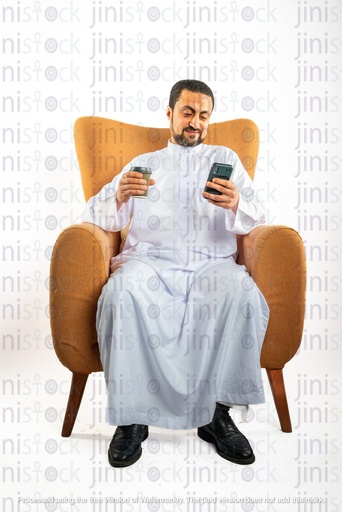 saudi khaliji man sitting on a chair checking his mobile phone and holding a coffee travel cup on the other hand