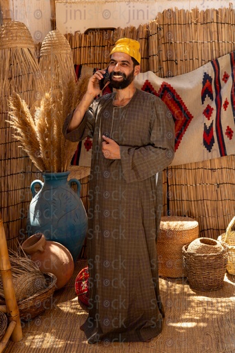An Egyptian farmer stands happy talking on the phone wearing a galabiya in a wicker hut 