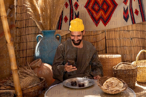 Egyptian man holding his phone smiling sitting in a hut 