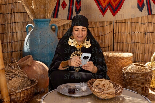 An Egyptian Bedouin woman in a wicker hut holding her phone