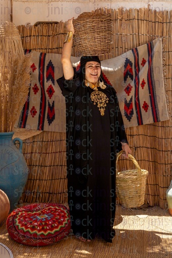 A laughing Bedouin woman stands holding a palm frond cage
