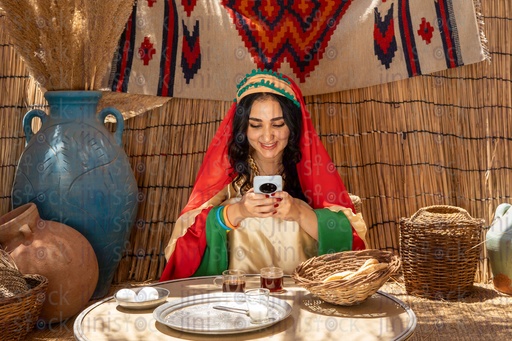 An Egyptian peasant woman sitting in a hut, looking at her phone and smiling 