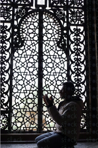 man praying in front of an artistic wooden window - stock image