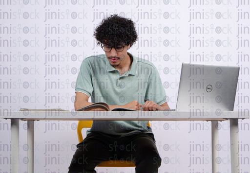 young man reading in booking while searching on his laptop - stock image